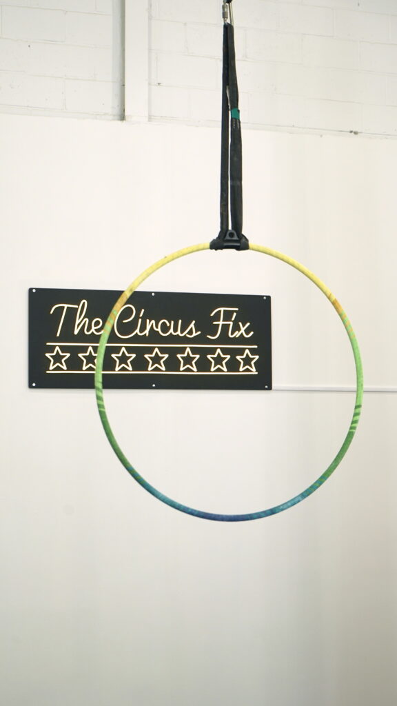 An aerial hoop hung in front of a sign that read The Circus Fix