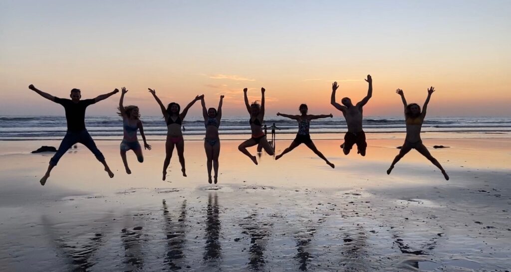 A group jumping in the air on the beach at sunset.